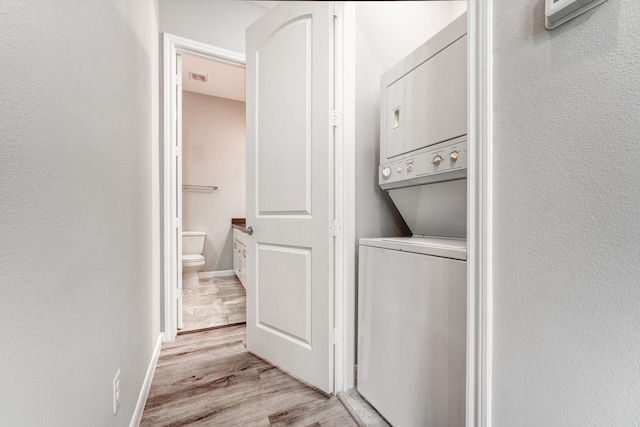 clothes washing area with light hardwood / wood-style flooring and stacked washer / drying machine