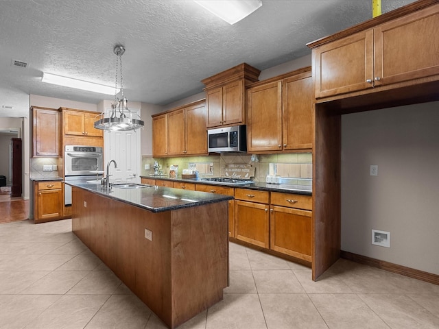 kitchen featuring decorative backsplash, appliances with stainless steel finishes, sink, an island with sink, and light tile patterned flooring