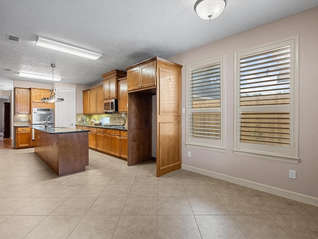 kitchen featuring appliances with stainless steel finishes, a textured ceiling, a kitchen island with sink, pendant lighting, and light tile patterned flooring