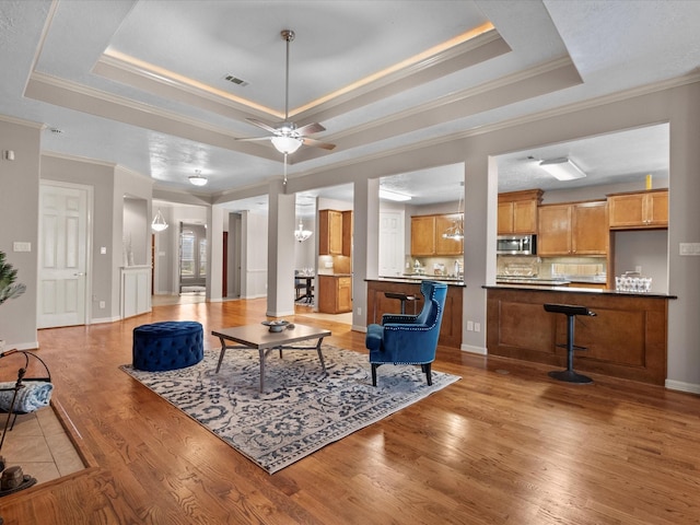 living room featuring ceiling fan, light wood-type flooring, ornamental molding, and a tray ceiling