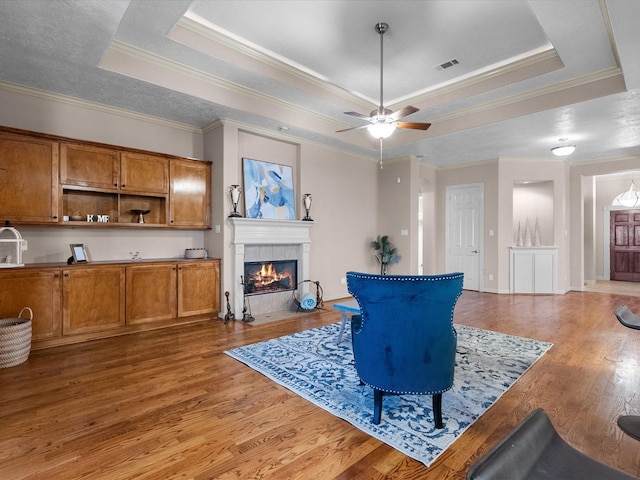 living room with hardwood / wood-style floors, crown molding, ceiling fan, a fireplace, and a tray ceiling