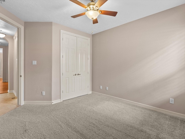 unfurnished bedroom featuring a textured ceiling, a closet, light colored carpet, and ceiling fan