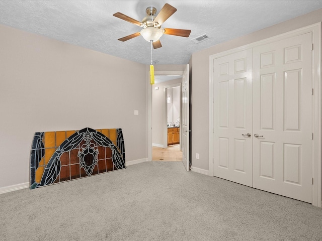 unfurnished bedroom with light carpet, a textured ceiling, a closet, and ceiling fan