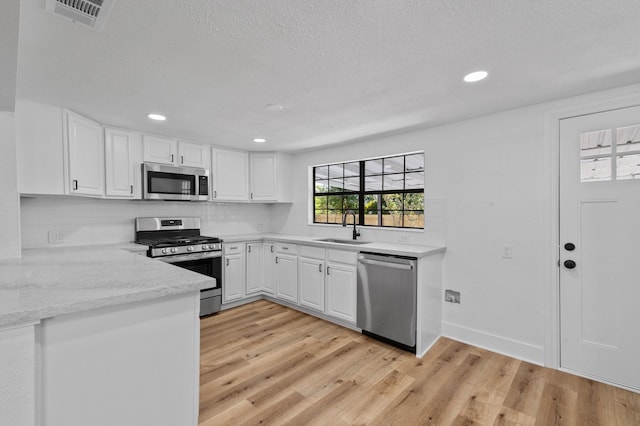 kitchen featuring light stone countertops, stainless steel appliances, sink, light hardwood / wood-style floors, and white cabinetry