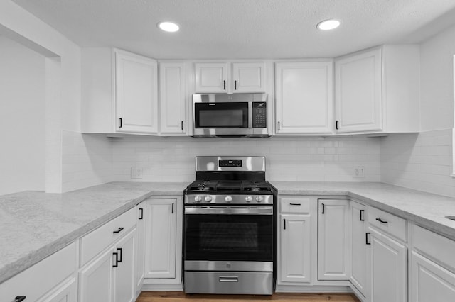 kitchen with white cabinets, appliances with stainless steel finishes, a textured ceiling, and tasteful backsplash