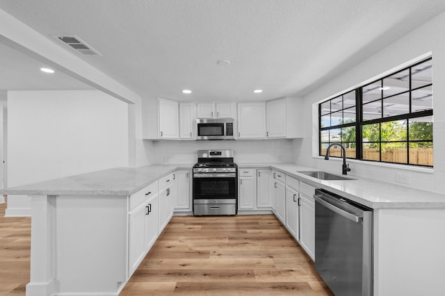 kitchen with kitchen peninsula, white cabinetry, light hardwood / wood-style flooring, and stainless steel appliances