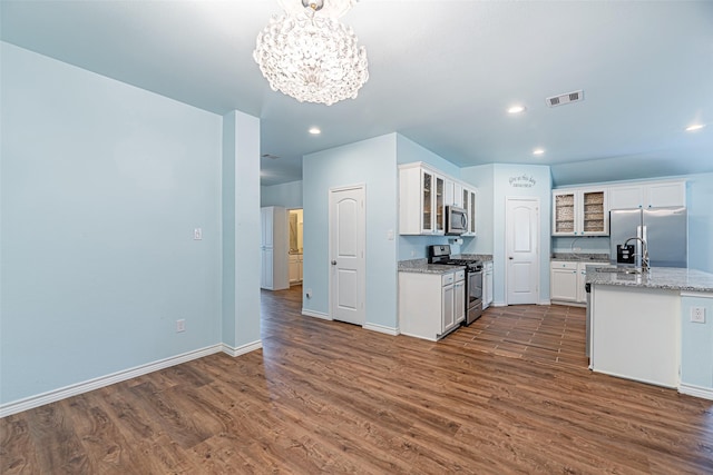 kitchen featuring light stone countertops, stainless steel appliances, dark wood-type flooring, white cabinets, and a chandelier