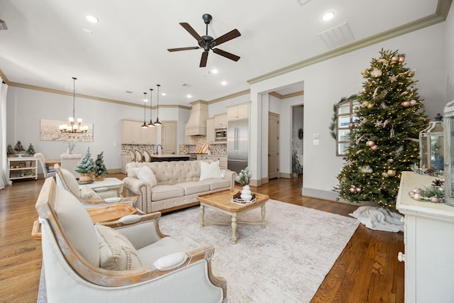 living room featuring wood-type flooring, sink, ceiling fan with notable chandelier, and crown molding