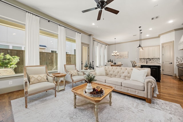 living room featuring hardwood / wood-style flooring, ornamental molding, and ceiling fan with notable chandelier