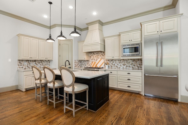 kitchen with a kitchen bar, hanging light fixtures, built in appliances, custom range hood, and a center island with sink