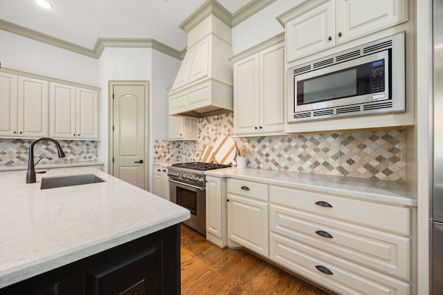 kitchen with premium range hood, appliances with stainless steel finishes, sink, hardwood / wood-style flooring, and crown molding