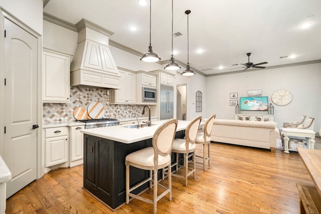 kitchen with stainless steel microwave, an island with sink, white cabinetry, sink, and hanging light fixtures