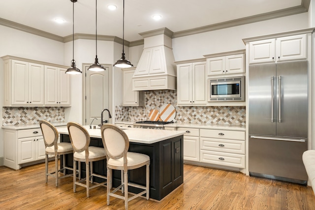 kitchen with a breakfast bar, built in appliances, an island with sink, decorative light fixtures, and custom exhaust hood