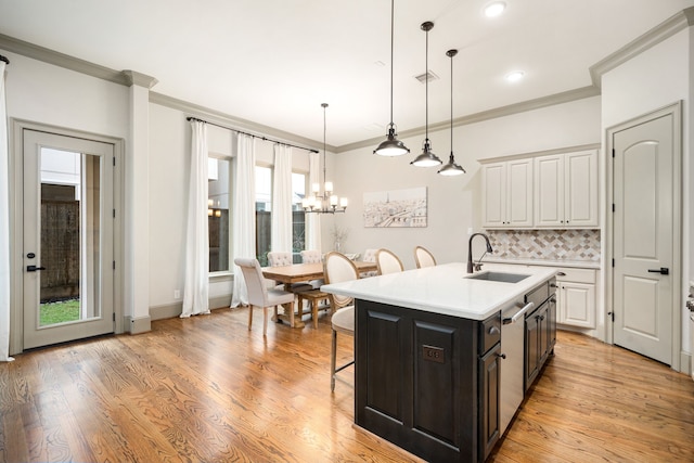 kitchen featuring pendant lighting, white cabinetry, an island with sink, sink, and a kitchen bar