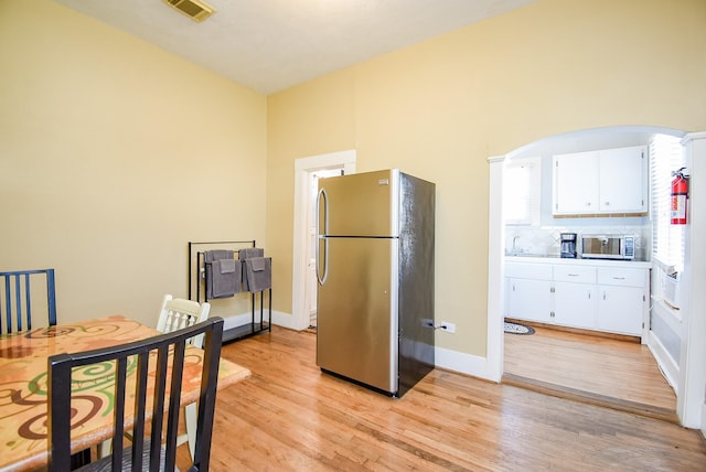 kitchen with a wealth of natural light, light wood-type flooring, white cabinetry, and appliances with stainless steel finishes