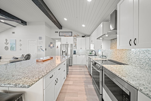 kitchen with light stone counters, a center island, appliances with stainless steel finishes, wall chimney range hood, and white cabinets