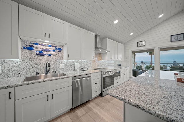 kitchen featuring vaulted ceiling, appliances with stainless steel finishes, sink, white cabinets, and wall chimney exhaust hood