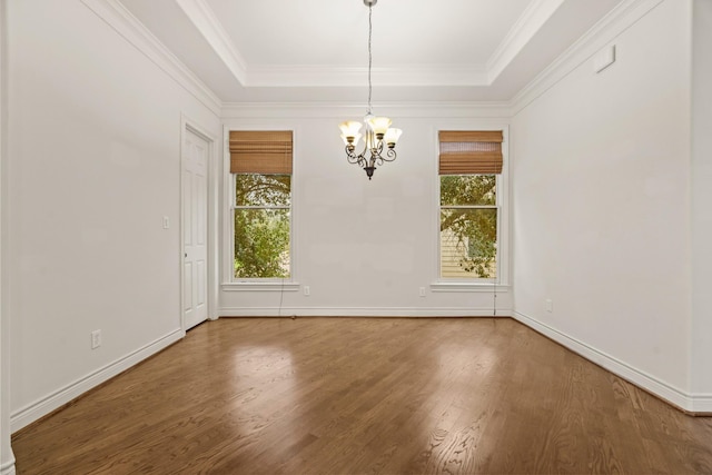 empty room featuring a raised ceiling, wood-type flooring, and an inviting chandelier