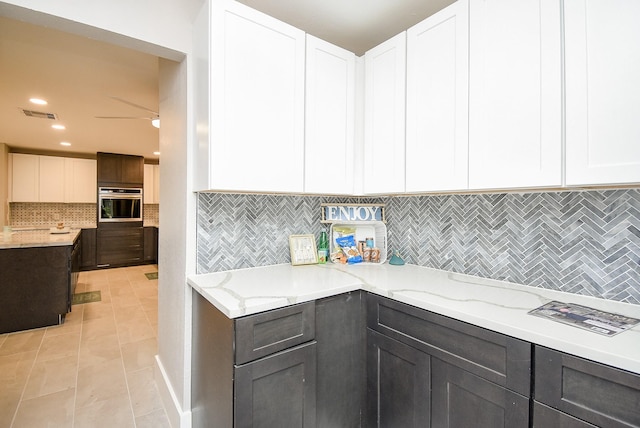 7618 Highmeadow Dr, Houston, TX 77063 - kitchen with stainless steel oven, light stone countertops, decorative backsplash, white cabinets, and light tile patterned floors