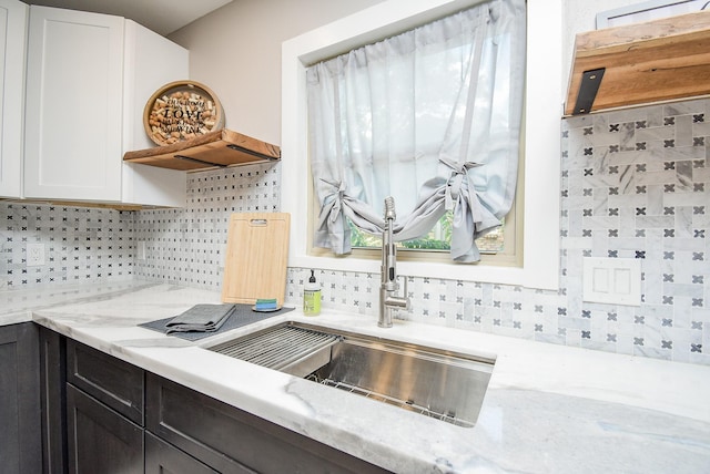 kitchen featuring tasteful backsplash, white cabinetry, sink, and light stone counters