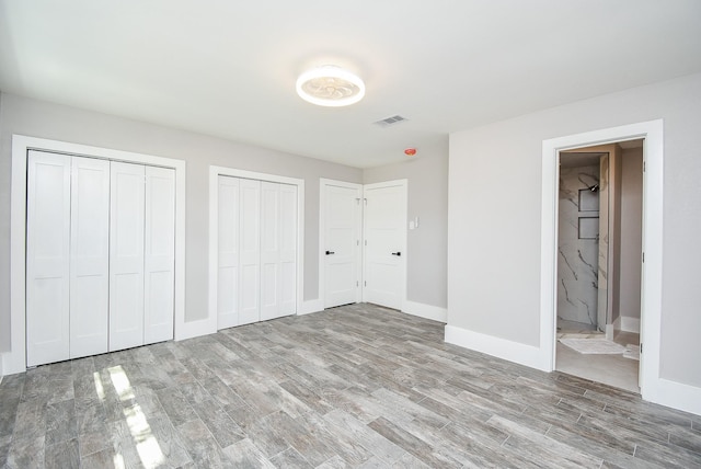 unfurnished bedroom with two closets, ensuite bathroom, and light hardwood / wood-style floors