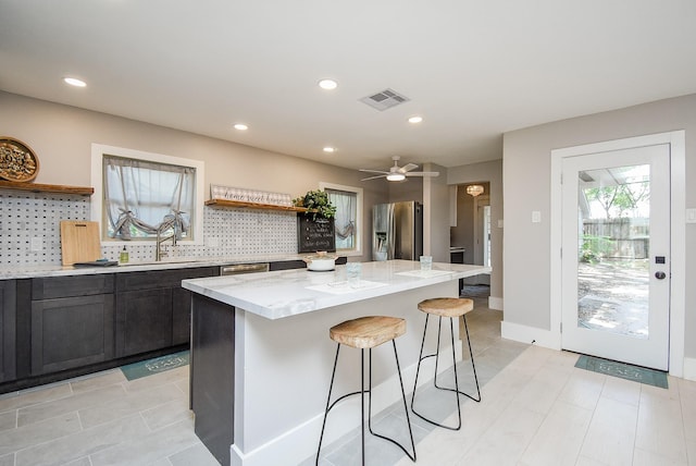 kitchen with backsplash, stainless steel fridge, a kitchen island, and light stone countertops