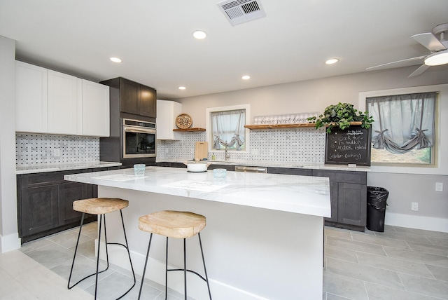 7618 Highmeadow Dr, Houston, TX 77063 - kitchen with stainless steel appliances, open shelves, light stone countertops, a breakfast bar area, and decorative backsplash