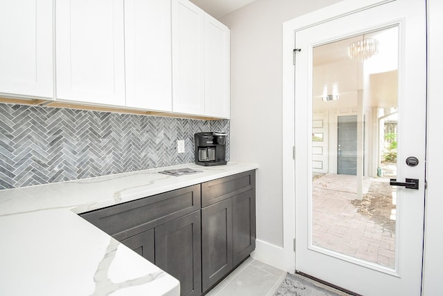 kitchen with white cabinets, decorative backsplash, dark brown cabinets, light stone counters, and a chandelier