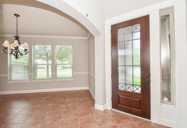 tiled foyer with ornamental molding and an inviting chandelier