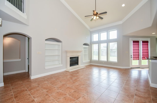 unfurnished living room with built in shelves, ceiling fan, crown molding, light tile patterned floors, and a high ceiling