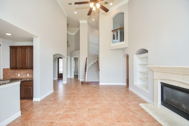 unfurnished living room with ceiling fan, built in features, light tile patterned floors, and a high ceiling