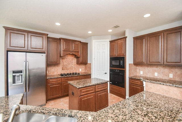 kitchen featuring a center island, light stone counters, decorative backsplash, light tile patterned floors, and black appliances