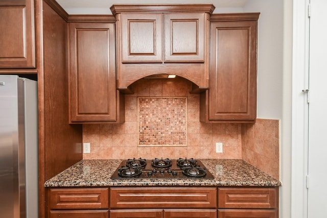 kitchen with tasteful backsplash, stainless steel refrigerator, black gas stovetop, and dark stone countertops