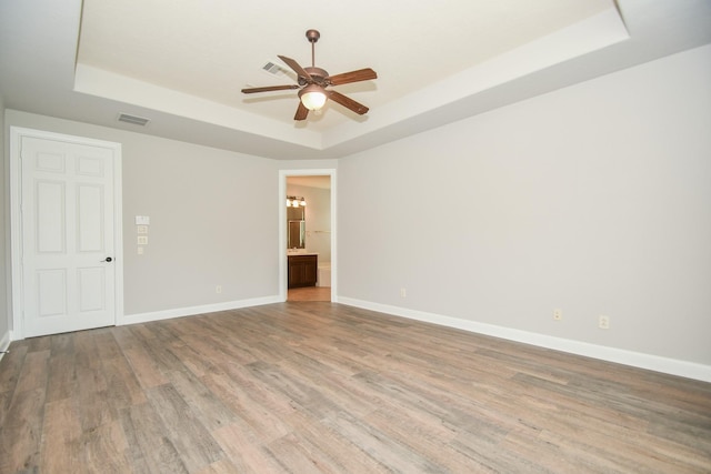 empty room featuring ceiling fan, light hardwood / wood-style floors, and a raised ceiling