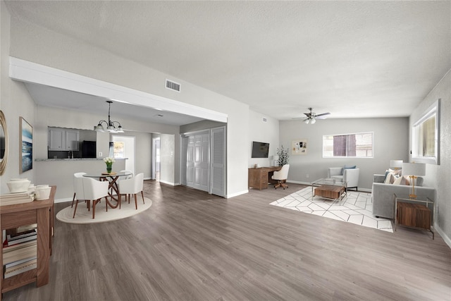 living room featuring a textured ceiling, ceiling fan with notable chandelier, and light wood-type flooring