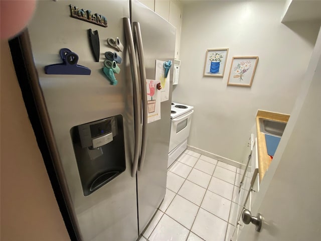 kitchen with sink, electric range, stainless steel fridge, light tile patterned floors, and white cabinetry