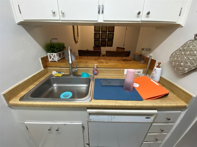 kitchen with white dishwasher, white cabinets, and sink