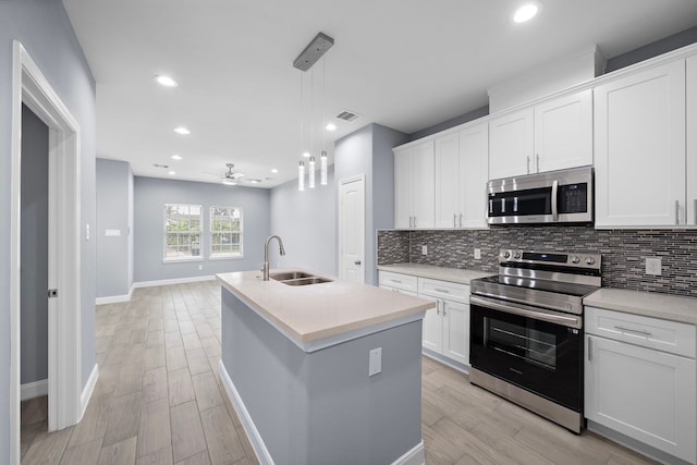 kitchen featuring appliances with stainless steel finishes, a kitchen island with sink, ceiling fan, white cabinets, and hanging light fixtures