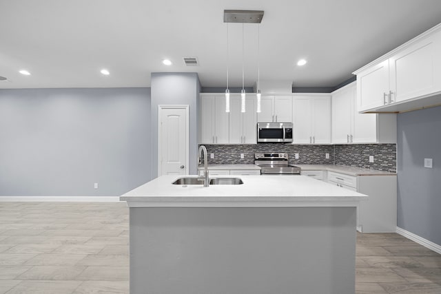 kitchen with a center island with sink, white cabinetry, hanging light fixtures, and appliances with stainless steel finishes