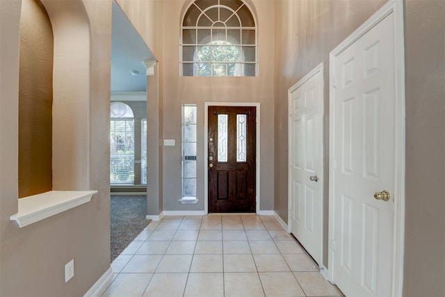 entryway featuring light tile patterned floors, a high ceiling, and ornamental molding