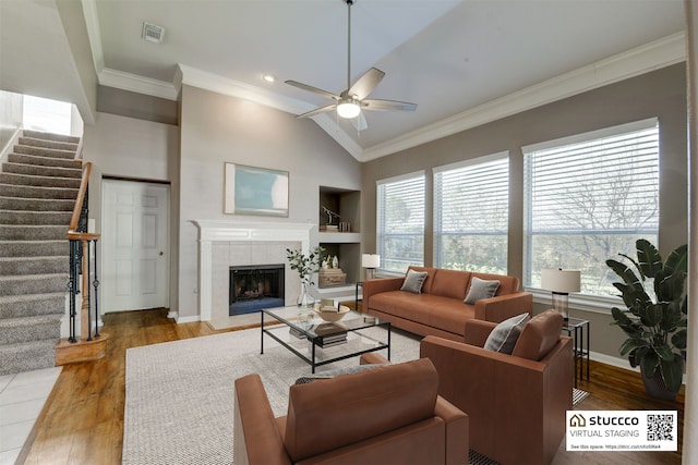 living room featuring ornamental molding, vaulted ceiling, ceiling fan, hardwood / wood-style floors, and a tiled fireplace