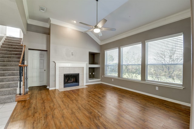 unfurnished living room featuring a tile fireplace, crown molding, ceiling fan, built in shelves, and wood-type flooring