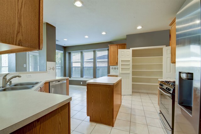 kitchen with sink, a kitchen island, light tile patterned floors, and appliances with stainless steel finishes