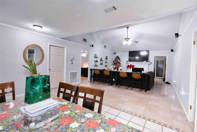 tiled dining room featuring ceiling fan, ornamental molding, and vaulted ceiling