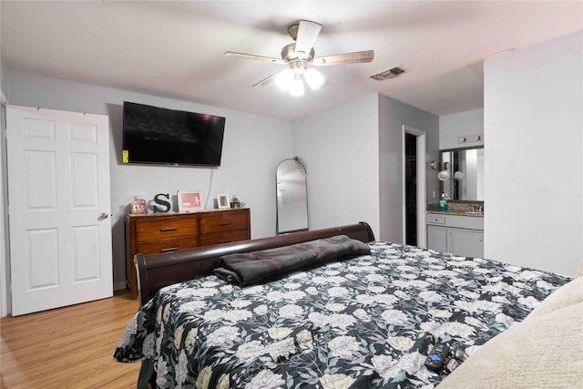 bedroom featuring light wood-type flooring, ensuite bath, ceiling fan, and sink