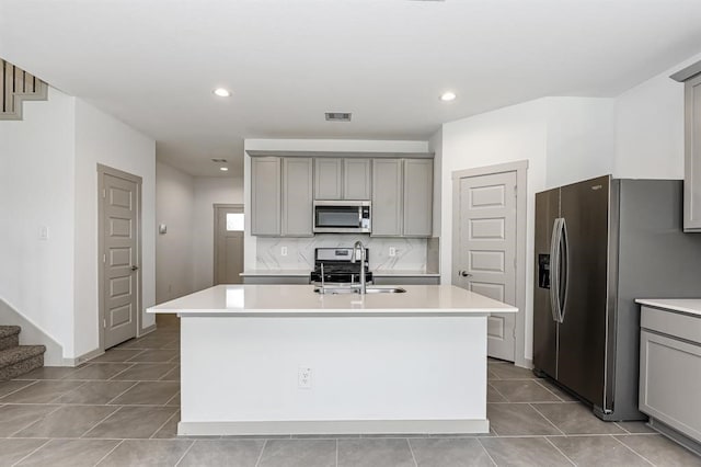 kitchen featuring visible vents, appliances with stainless steel finishes, a kitchen island with sink, gray cabinetry, and a sink