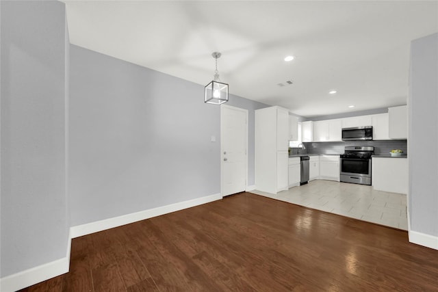 kitchen with appliances with stainless steel finishes, light wood-type flooring, white cabinetry, and pendant lighting