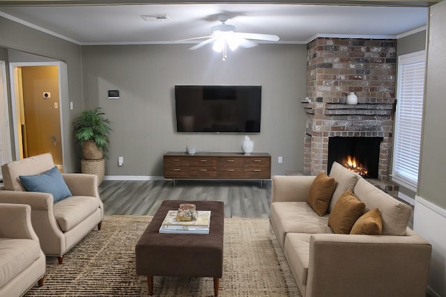 living room with ceiling fan, dark hardwood / wood-style flooring, crown molding, and a brick fireplace