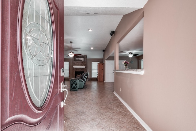 tiled foyer entrance featuring ceiling fan and a fireplace