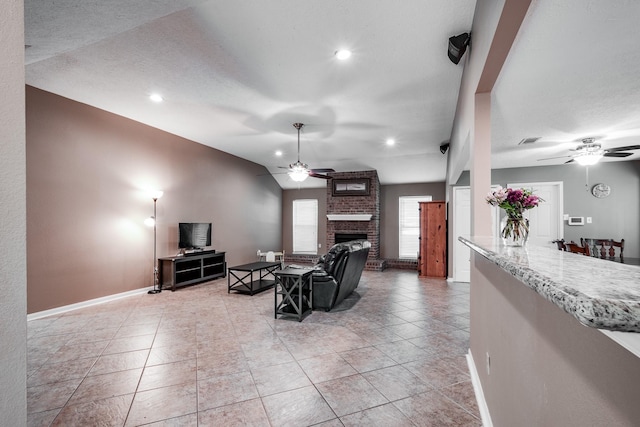 tiled living room with a fireplace, a textured ceiling, vaulted ceiling, and ceiling fan